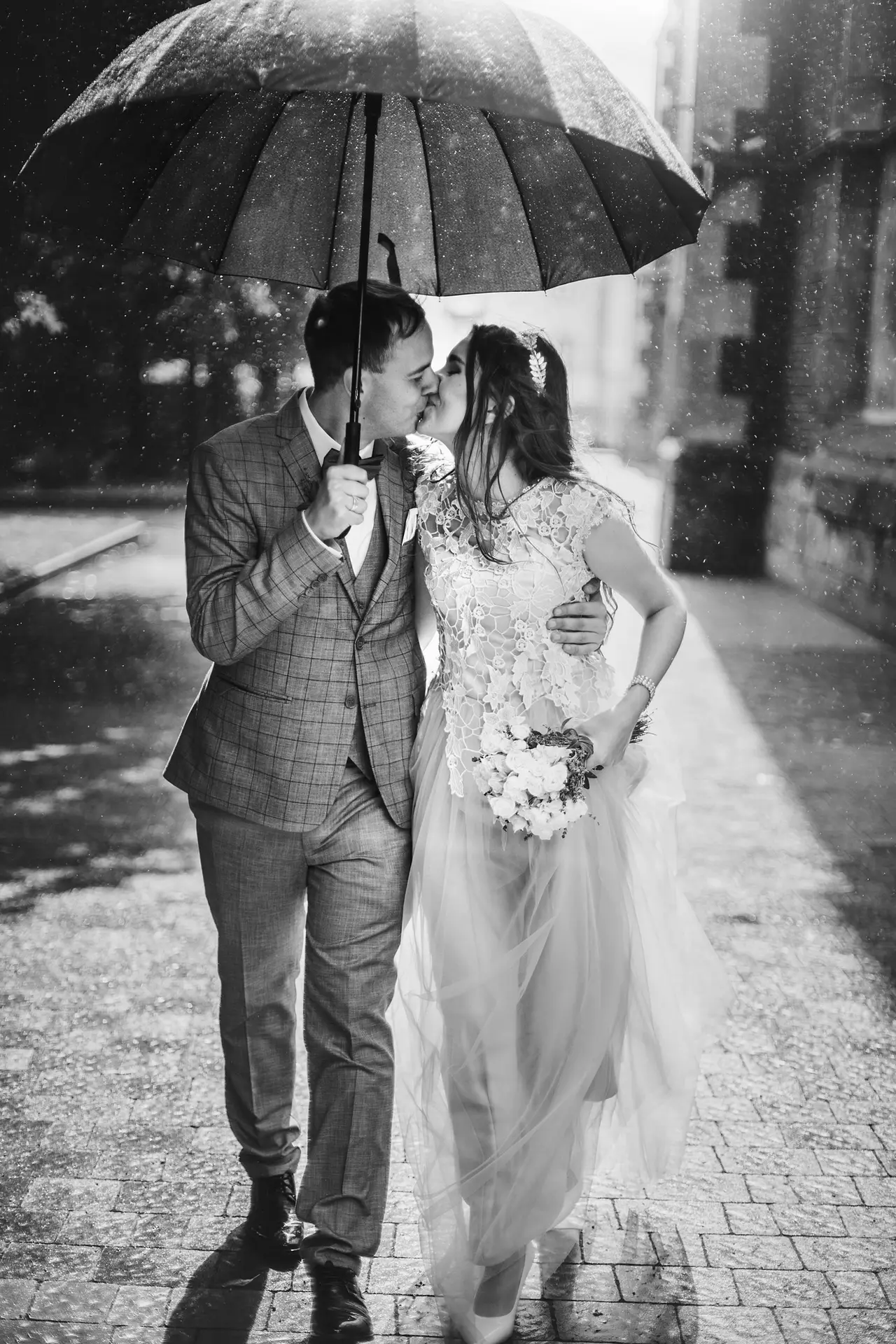 Beautiful wedding couple embracing together under umbrella in sunny rainy street